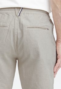 Beige stripete bukser med avslappet passform, med to baklommer og en subtil tekstur. Akcentstripe i marineblå langs lomme kantene.