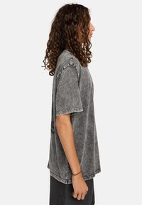 Camiseta de mezclilla gris con un ajuste relajado, mangas cortas y costuras contrastantes. La tela tiene un aspecto texturizado y desgastado.