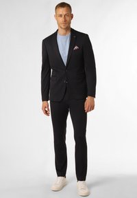 Schwarzer Anzug mit Revers und zwei Knöpfen, kombiniert mit einem hellblauen T-Shirt und weißen Sneakers. Enthält ein gemustertes Einstecktuch.