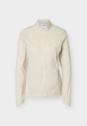 Jachetă ușoară bej deschis pentru femei, cu fermoar, guler drept și mansete elastice, cu un mic logo alb pe pieptul stâng.