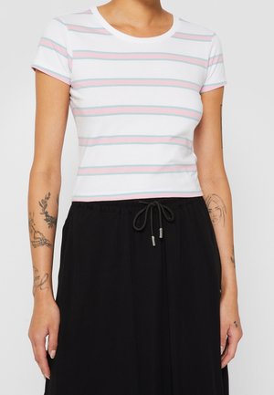 Person iført en hvid kort t-shirt med pink og blå striber og et sort højtkalvet skørt med snøre i taljen. Tatoveringer synlige på armene.