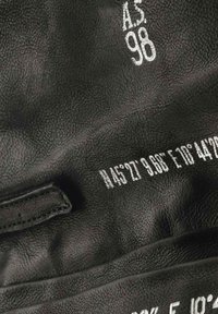 Materiale in pelle nera con superficie testurizzata. Presenta testo in rilievo bianco e coordinate geografiche. Design semplice senza accenti aggiuntivi.