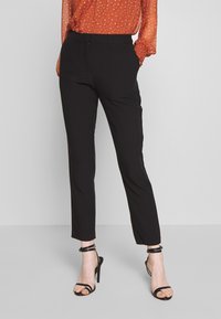 Sorte skreddersydde bukser med slim fit, flat front og beltehemper, kombinert med sorte høye hæler. Glatt stoff, minimalistisk design.