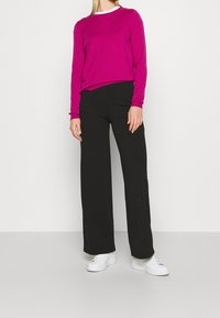 Fuchsia Langarmpullover, schwarze weite Hosen und weiße Sneakers. Glatte Textur, schlichtes Design, keine sichtbaren Muster oder Verzierungen.