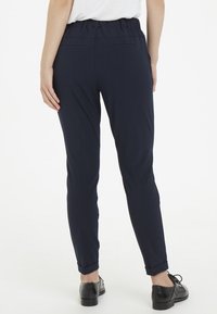 Pantalons bleu marine fuselés avec une taille élastique, dotés de poches arrière et d'ourlets à revers, fabriqués en tissu léger et lisse.