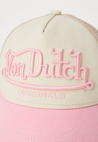 Lys beige caps med en rosa buet skjerm, med fremtredende rosa brodert tekst "Von Dutch" og "ORIGINALS" på forsiden.