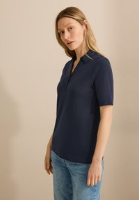 Navyblauwe polo met een gladde stof, voorzien van een kraag en korte mouwen. Eenvoudig ontwerp zonder zichtbare patronen of accenten.