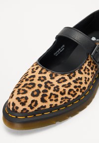 Schoen met panterprint, voorzien van een zwarte leren band en een ronde neus. Heeft een rubberen zool met gele stiksels en een gestructureerd oppervlak.