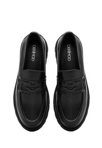 Mocassins en cuir noir avec une surface lisse, un bout arrondi et une sangle décorative avec un design découpé subtil. Semelle en caoutchouc épaisse.