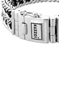 Bracciale in metallo argentato con design intrecciato e chiusura a gancio. Il componente metallico ha un'etichetta nera con la scritta "Kuzzoi".