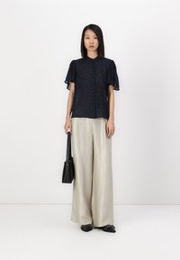 Blusa navy a maniche corte con chiusura a bottoni e maniche arricciate, abbinata a pantaloni palazzo beige chiaro e accessori neri.