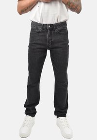 Jeans in denim nero con design a taglio slim, stile a cinque tasche, bottoni in argento e sfumature delicate. Abbinati a sneakers bianche.