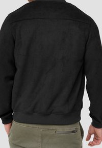 Veste en daim noir avec un col rond, des poignets et un ourlet côtelés, présentant une texture lisse et un design simple. Vue de dos montrée.