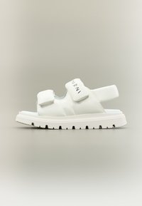 Λευκά δερμάτινα σανδάλια με ρυθμιζόμενες λουρίδες κλεισίματος, παχύ λευκό καουτσούκ πέλμα και ανάγλυφη λεπτομέρεια λογοτύπου. Μινιμαλιστικός σχεδιασμός και ανοιχτό στυλ.