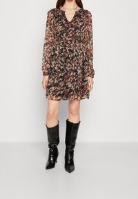 Ohut musta kukallinen mekko pitkillä hihoilla, V-pääntiellä ja kerätyllä vyötäröllä. Yhdistettynä mustiin polvensuuhun ulottuviin kiiltäviin saappaisiin.