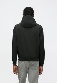 Juodas džemperis, pagamintas iš lygaus audinio, su aukštu apykakle, reguliuojamais raišteliais ir raištinėmis rankovėmis bei apvadu. Dėvimas su pilkais džinsais.