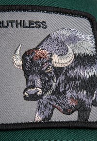 Schwarzes und graues gesticktes Büffelpiktogramm auf einem rechteckigen grauen Hintergrund mit dem Text "RUTHLESS" darüber. Schwarzer Rand auf dem Patch.