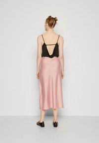 Svart sleeveless topp med lav rygg og hvite prikker, kombinert med et rosa satin midi-skjørt, iført svarte slip-on sko.