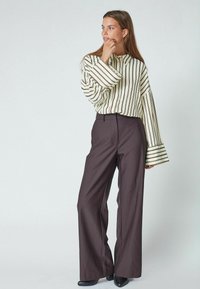 Chemise à rayures crème à manches longues et larges, accompagnée d'un pantalon large taille haute marron foncé. Des chaussures noires complètent le look.