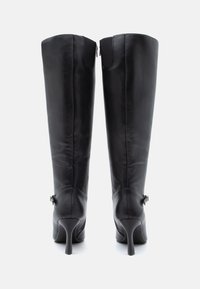 Alti stivali in pelle nera con un design elegante, tacchi a spillo e chiusura con zip. Presentano un piccolo accento metallico vicino al tallone.