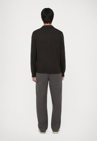 Suéter de punto marrón oscuro con cuello tipo polo, combinado con pantalones de pierna ancha grises que tienen bolsillos laterales y un corte holgado.