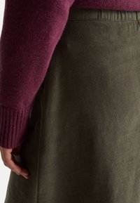 Pletený svetr v burgundské barvě a olivově zelená manšestrová sukně. Obsahuje žebrované manžety a měkkou texturu, s detailním pohledem na látku a design.