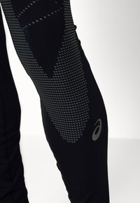 Leggings de sport noirs avec un motif texturé gris, un accent rond sur le bas de la jambe et des détails cousus le long des coutures.