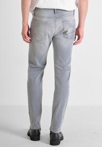 Jeans de mezclilla de un gris claro con corte ajustado, que cuentan con cinco bolsillos y una cintura estándar, combinados con zapatos negros. Textura de tela suave.