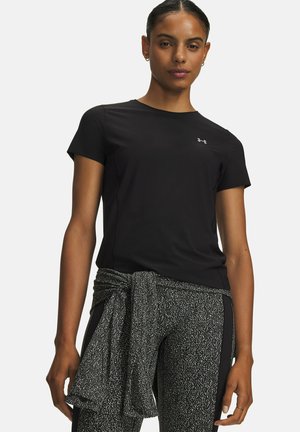 Vrouw die een zwart T-shirt met korte mouwen en een zwart-witte broek met patroon draagt, met een bijpassend jasje om haar middel gebonden.