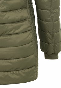 Manche et côté d'une veste matelassée verte olive avec surpiqûres horizontales et poignet élastique à la manche.