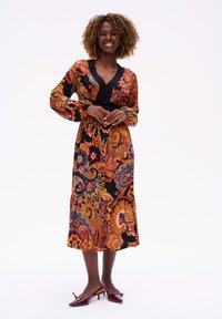 Langemouwen V-hals jurk in een levendig bloemenpatroon van oranje, roze en turquoise op een zwarte achtergrond. Glad materiaal met een elastische taille.