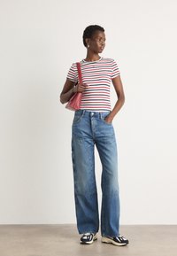 T-shirt rayé rouge et blanc associé à un jean en denim bleu à jambes larges. Les accessoires incluent un sac à main rose et des baskets noir et blanc.