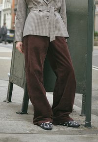 Karierter Blazer mit einem taillierten Gürtel, kombiniert mit burgunderroten Cordhosen mit weiter Beinform und spitzen schwarzen Flats mit silbernen Nieten.