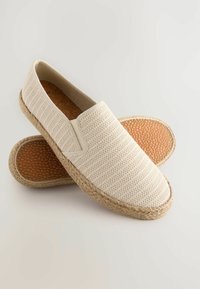 Beige slip-on sko med vævet tekstiloverdel, naturlig jutebrim og struktureret gummisål, der har en let polstret indersål.