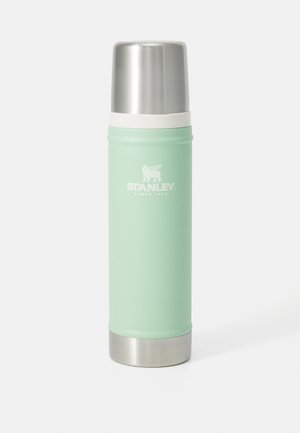 Lichtgroene roestvrijstalen Stanley thermosfles met een zilveren deksel en basis, rechtopstaand op een witte achtergrond.
