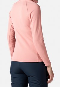 Haut ajusté à manches longues en doux matériau rose clair, avec un col haut et des détails de couture subtils, associé à un pantalon bleu marine foncé.