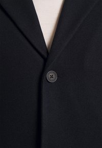 Schwarzer Wollblazer mit einem Reverskragen, Ein-Knopf-Verschluss und glatter Textur, im minimalistischen Design.