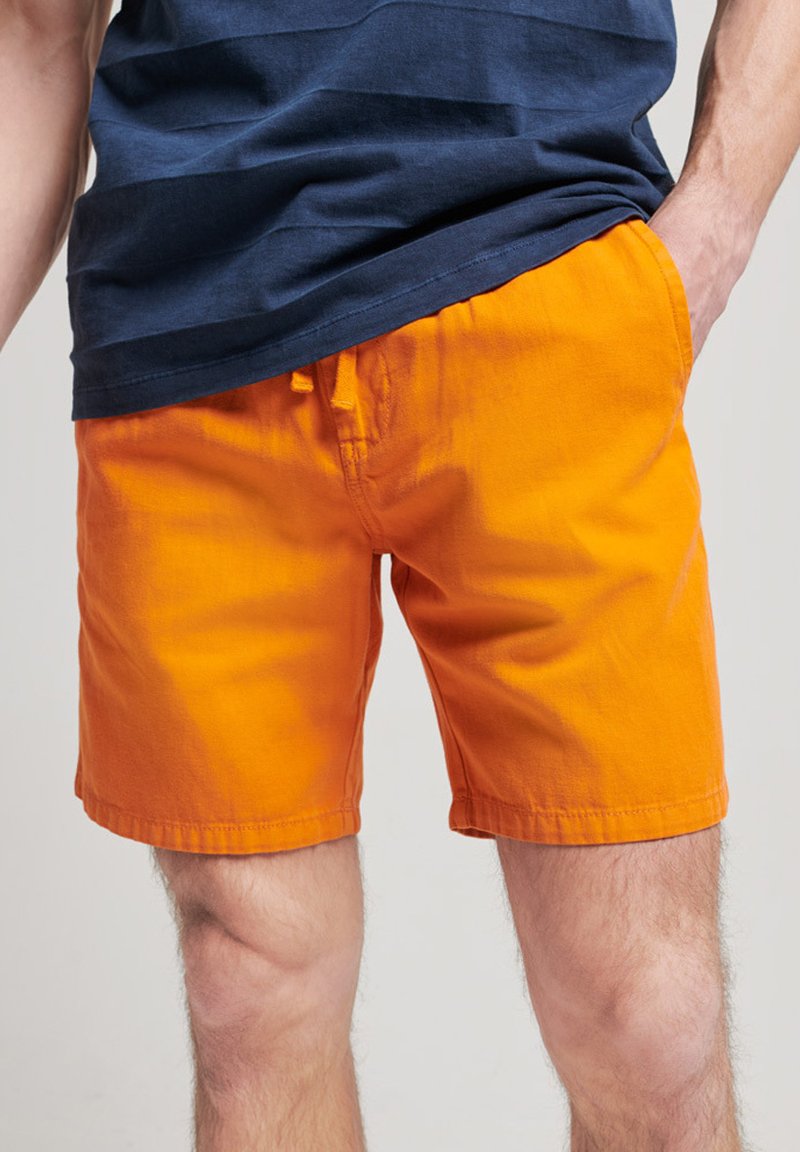 Pomarańczowe bawełniane szorts z elastycznym paskiem w talii, charakteryzujące się jednolitym kolorem. Materiał wygląda na lekki i lekko teksturowany.