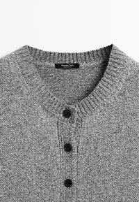 Maglione grigio a maglia con scollatura rotonda, colletto a coste e tre bottoni neri sul davanti, con una finitura in tessuto testurizzato.