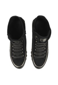 Un paio di sneakers nere alte con spesse stringhe nere, zip laterali e sofisticata bordatura bianca lungo la suola, viste dall'alto.