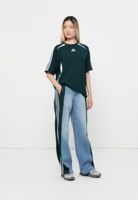 Dark green athletic shirt with white stripes, paired with light blue wide-leg jeans featuring dark green side panels and gray sneakers.