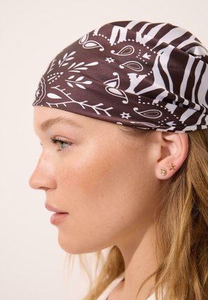 Ung kvinde i profil iført et brunt og hvidt mønstret hovedtørklæde og små øreringe af guldsnegle og søstjerner.