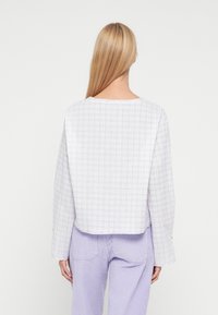 Lysegrå ternet top med lange ærmer og rund halsudskæring. Stoffet virker tekstureret, cropped længde, kombineret med lyse lilla bukser.