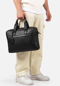 Porta documenti in pelle nera con doppie maniglie superiori, superficie texturizzata, dettaglio logo impresso e forma rettangolare elegante.