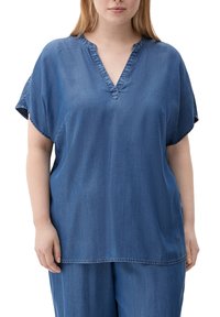 Denim top in medium blue with short sleeves, V-neck, and a relaxed fit. Features stitching along the neckline and hem for detail.