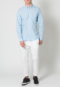 Hellblau karierte Button-up-Bluse mit langen Ärmeln, mit Taschendetail, kombiniert mit weißen hochgekrempelten Hosen und dunklen Sneakers.