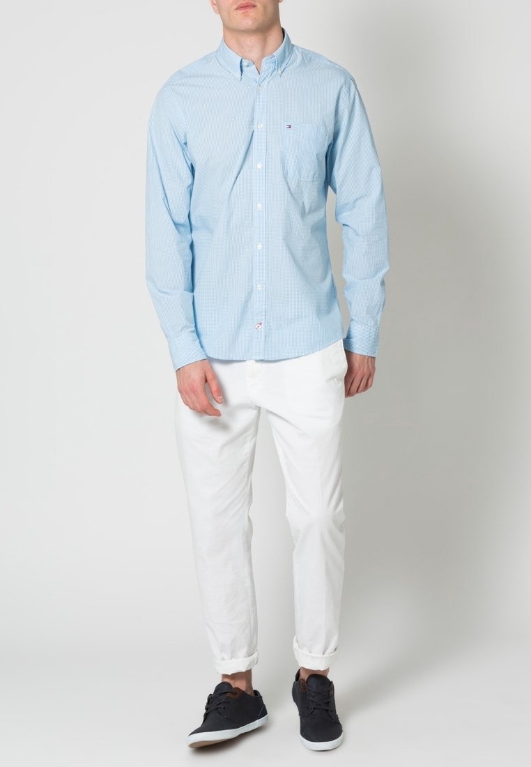 Hellblau karierte Button-up-Bluse mit langen Ärmeln, mit Taschendetail, kombiniert mit weißen hochgekrempelten Hosen und dunklen Sneakers.