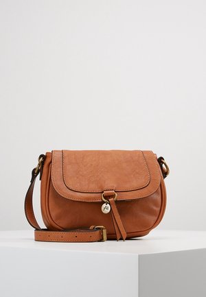 Braune Ledertasche mit verstellbarem Schulterriemen, Klappverschluss und kleinem runden Metallanhänger an der Fransenverzierung auf der Vorderseite, auf einer weißen Oberfläche platziert.