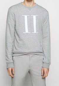 Szara bluza wykonana z miękkiego materiału, z wyraźnym białym nadrukiem "II" na przodzie. Mankiety i pas ze ściągaczem.