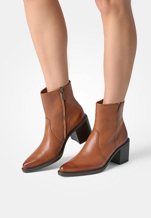 Bottines en cuir marron avec un bout pointu, fermeture éclair sur le côté et talon bloc. Texture lisse et détails de couture minimaux.